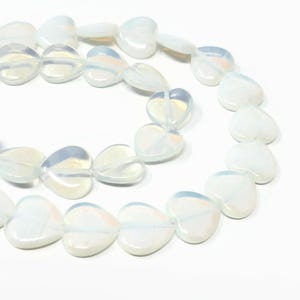 May include: A strand of white opal heart-shaped beads. The beads are iridescent and have a translucent quality.