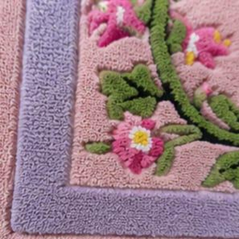 May include: A textured rug featuring a light pink base with a lavender border. The centre displays a raised, tufted floral pattern with green vines, green leaves, and pink flowers with white and yellow centres, created with a looped pile technique.