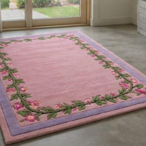 May include: A rectangular area rug featuring a solid pink centre field surrounded by a decorative border of green vines and pink flowers. The rug is framed by a light purple outer border, creating a distinct contrast against the pink interior.