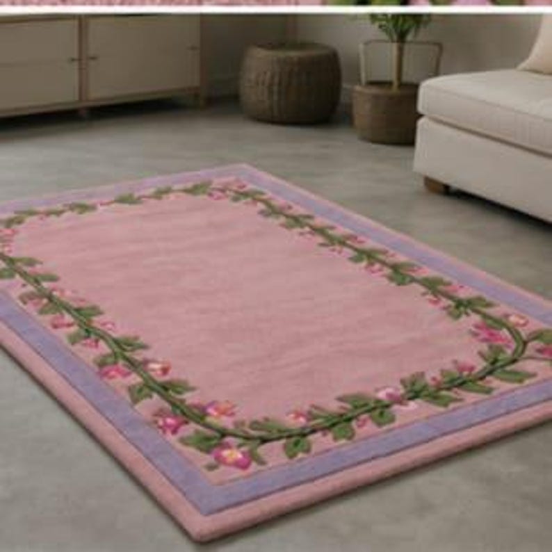 May include: A rectangular area rug featuring a solid pink centre field surrounded by a decorative border of green vines and pink flowers. The rug is framed by a light purple trim that runs along the entire perimeter of the rectangular design.