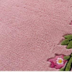 May include: A textured dusty pink fabric surface featuring a decorative border with embroidered green leaves and small pink flowers with white petals and yellow centres. The material has a dense, looped pile construction throughout the main area.