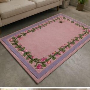 May include: A rectangular area rug featuring a solid light pink centre bordered by a decorative vine pattern with green leaves and small pink flowers. The rug is framed by a lavender border and finished with a light pink outer edge trim.