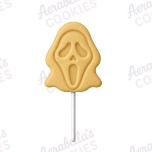 May include: A light tan biscuit shaped like a ghost mask with a screaming expression, featuring hollowed-out eyes and a mouth, attached to a thin white stick. The biscuit has a smooth, textured surface and is centred against a white background.