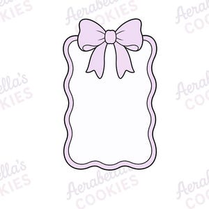 May include: A light purple cookie cutter shaped like a rectangular tag with wavy sides and a decorative bow at the top. The outline is defined by a thick purple border, and the centre is white. The text Aerabella's COOKIES appears in the background.