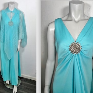 May include: A light blue sleeveless maxi dress with a large jeweled embellishment on the bodice. The dress has a V-neckline and a flowing skirt. It is paired with a matching sheer cape.