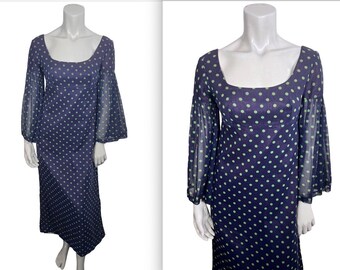 May include: A navy blue, floor-length dress with a square neckline and long, sheer, bell sleeves. The dress is patterned with small, light green polka dots. The dress is displayed on a mannequin.