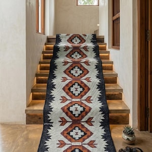 May include: A stair runner rug with a geometric pattern in shades of black, white, and brown. The runner is placed on wooden stairs with warm lighting. The rug features a repeating diamond and arrow design.