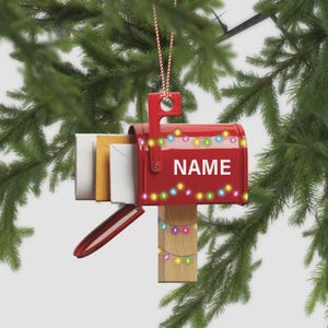 May include: A red mailbox Christmas ornament with the word "NAME" in white. The mailbox has a string of colorful lights across the top and down the wooden post. Several envelopes are visible inside the mailbox.