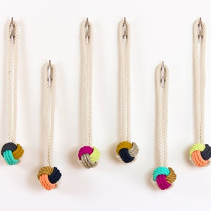 May include: Six decorative rope wall hooks with colorful knotted accents. Each hook features a natural rope loop attached to a metal clip, with a decorative knot in shades of teal, pink, yellow, and orange. The hooks are displayed against a white background.