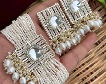 May include: Elegant white pearl and rhinestone jewelry set. The set includes a bracelet and matching earrings. The earrings and bracelet feature a square design with a large, clear rhinestone center and dangling pearls. The jewelry is set against a neutral background.