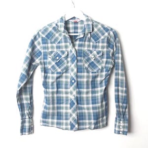 May include: A blue, green, and white plaid button-down shirt with long sleeves. The shirt has two chest pockets with button closures and a classic collar. The cuffs have button closures. The shirt is hanging on a white hanger.