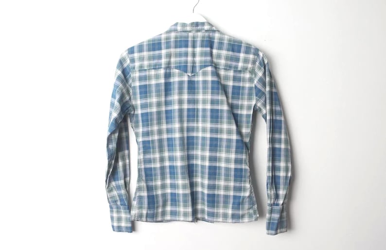 May include: Blue and white plaid long-sleeve shirt hanging on a white hanger. The shirt has a classic button-down design with a pointed collar and buttoned cuffs. The plaid pattern features shades of blue, white, and green.