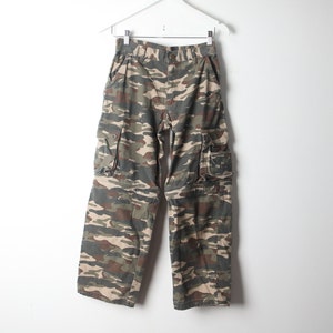 May include: Camouflage cargo pants with multiple pockets. The pants are a mix of brown, green, and beige.
