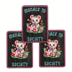 May include: Three embroidered patches with a black background and a pink border. Each patch features a cute pink teddy bear with a bow, surrounded by flowers, and the text "MENACE TO SOCIETY".