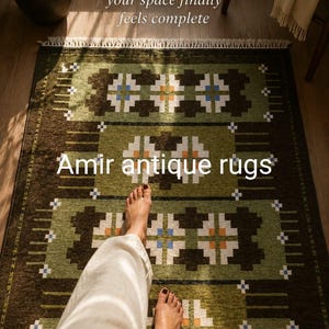 May include: A rectangular area rug featuring a geometric pattern in shades of olive green, dark brown, white, and blue, with white fringe at the ends. The text reads: POV: your space finally feels complete and Amir antique rugs.