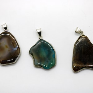 Peut inclure: Trois pendentifs en pierres précieuses avec des bélières argentées. Les pendentifs ont des formes irrégulières et sont dans les tons marron, vert et noir. Les pierres sont serties dans un cadre en métal argenté.