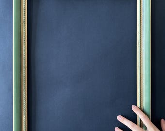 May include: A rectangular picture frame with a green painted finish and gold trim. The frame has a beaded inner edge and is set against a dark blue background.