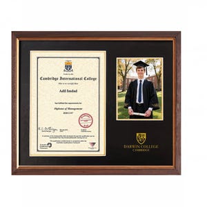 Op de afbeelding: Een donkerhouten lijst met een diploma van het Cambridge International College voor Adil Imdad, een Diploma of Management, en een foto van een afgestudeerde in toga en baret. De zwarte passe-partout bevat het gouden Darwin College logo.