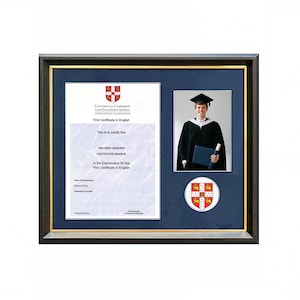 Könnte beinhalten: Gerahmtes Zertifikat und Foto. Das Zertifikat lautet "First Certificate in English" von der Universität Cambridge. Der Rahmen ist dunkelbraun mit einem goldenen Innenrand. Ein Foto eines Absolventen in Robe und Hut ist enthalten.