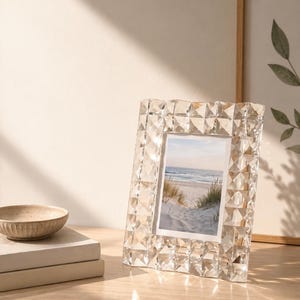 May include: A rectangular picture frame with a clear, faceted, geometric glass border that reflects light. The frame holds a photograph of a sandy beach with dunes and the ocean. The design features a repeating pyramid-like pattern.