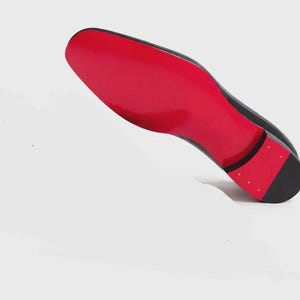 May include: Black dress shoe with a vibrant red sole. The shoe is angled, showcasing the glossy red underside and the sleek, dark upper. The heel features a black cap with small, gold-colored studs.