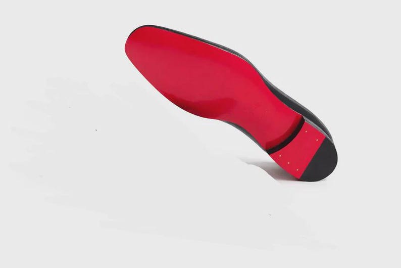May include: Black dress shoe with a vibrant red sole. The shoe is angled, showcasing the glossy red underside and the sleek, dark upper. The heel features a black cap with small, gold-colored studs.