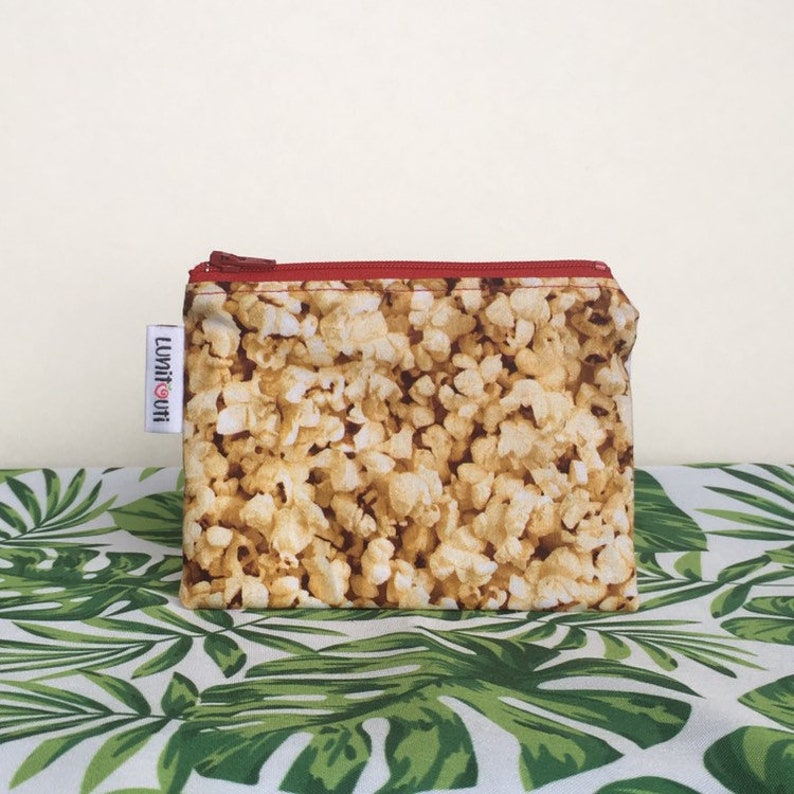 May include: A small zippered pouch with a red zipper and a popcorn print. The pouch has a white label with the text "LUMI&CO" in black.