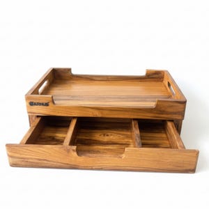 May include: A wooden desk organizer with a top tray and a pull-out drawer with three compartments. The organizer is made of light brown wood and features the brand name "GARNUS" on the front.