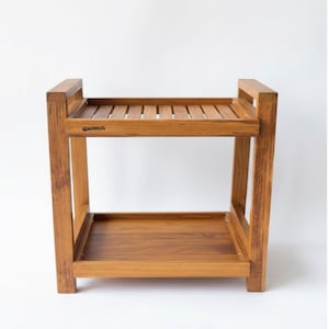 May include: A two-tiered wooden shelf with a natural finish. The top shelf has a slatted design, while the bottom shelf is solid. The frame is rectangular with vertical supports and the brand name "GARHUS" is visible on the side.