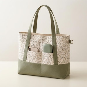 May include: A tote bag featuring a cream-colored fabric with a small brown floral pattern, accented by solid olive green fabric on the base and handles. The front includes two exterior pockets containing a smartphone and a small green case.