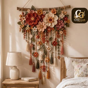 May include: A wall hanging featuring a collection of crocheted flowers in shades of rust, cream, and sage green, suspended from a natural wooden branch. The arrangement includes various floral shapes, leaves, and dangling yarn tassels with beads.