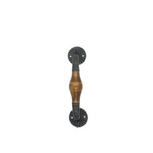 Könnte beinhalten: Ein Türgriff mit einem mittigen, glatten, hellbraunen Holzgriffstück, das von dunklen, texturierten Metallenden flankiert wird. Der Griff ist oben und unten mit runden, schwarzen Metallmontageplatten befestigt, die ein strahlenförmiges Muster aufweisen.