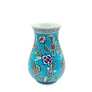 Könnte beinhalten: Eine Keramikvase mit helltürkisfarbenem Hintergrund und einem wiederkehrenden Blumenmuster in Rot, Weiß und Dunkelblau. Der Hals der Vase ist mit einem geometrischen Bordürenmuster in Dunkelblau und Weiß verziert, der Rand ist weiß.