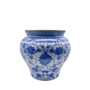 Puede incluir: Un jarrón de cerámica abombado con una base blanca decorada con intrincados patrones florales y vegetales en azul. El diseño incluye un borde detallado alrededor de la boca y un motivo botánico repetitivo en toda la superficie exterior.