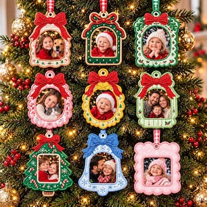 May include: A collection of nine embroidered fabric photo frame ornaments hanging on a Christmas tree. Each ornament features a unique shape, including bells, trees, and scalloped rectangles, decorated with red bows and festive patterns.