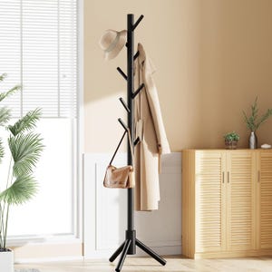 May include: A black coat rack with multiple branches for hanging items. A beige hat, coat, and purse are displayed on the rack. The rack has a tripod base and is placed in a room with a window and wooden cabinet.