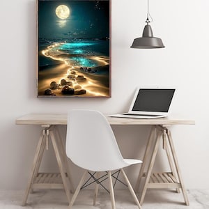 May include: A framed art print depicts a moonlit beach scene. The artwork features a bright full moon, a glowing path of light across the water, and a sandy shore with illuminated rocks. The print is displayed above a wooden desk with a laptop and a white chair.