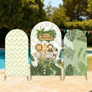May include: Three arched backdrop panels with a jungle theme. The central panel features a wooden sign that reads "Karren's Wild One" with cartoon animals in a jeep. The other panels have a light green zigzag pattern and a green leaf design.
