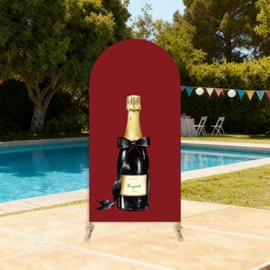 Puede incluir: Un letrero decorativo con una ilustraci&oacute;n de acuarela de una botella de champ&aacute;n con un lazo negro y detalles dorados. El letrero est&aacute; sobre un fondo rojo oscuro, con una piscina y un entorno al aire libre en el fondo.