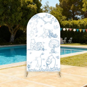 Puede incluir: Un telón de fondo blanco en forma de arco con ilustraciones en línea azul de Winnie the Pooh y sus amigos. El telón de fondo está sostenido por un soporte de metal dorado y está instalado al aire libre cerca de una piscina y una fiesta.