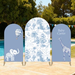 Può includere: Fondale per baby shower a tre pannelli con tema azzurro e bianco. I pannelli presentano un elefante, una mongolfiera, una giraffa e un motivo toile de Jouy con animali e alberi. Il pannello di destra ha il testo "Baby Carter".