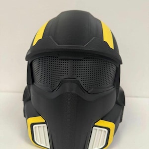 May include: A matte black helmet featuring a prominent visor with a fine mesh texture, two vertical yellow stripes extending over the top, and two white rectangular vents positioned on the lower sides framed by yellow accents.