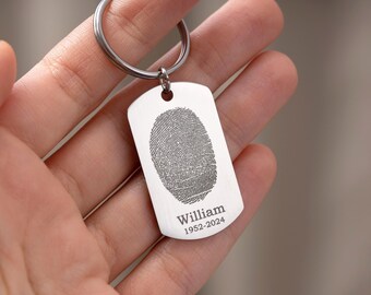 May include: A silver-colored keychain tag with a fingerprint design and the name "William" and the years "1952-2024" engraved on it. The tag is held by a person.