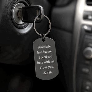 May include: A dark gray dog tag keychain with a silver key ring attached to a car key in the ignition. The tag has the engraved message: "Drive safe handsome. I need you here with me. I love you. -Sarah."
