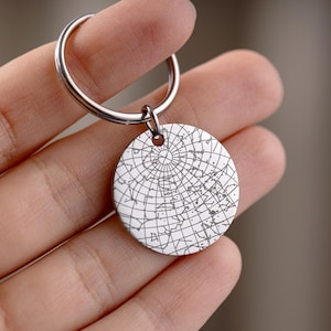 May include: A silver keychain with a round pendant featuring a detailed star map design. The pendant is attached to a silver keyring. The design is a network of lines and dots.