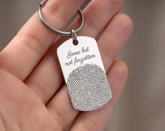 May include: A silver-colored keychain tag with the engraved words "Gone but not forgotten" above a fingerprint design. The tag is attached to a silver keyring. The keychain is held in a person's hand.
