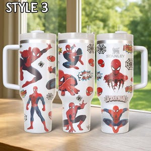 May include: Three white insulated tumblers with Spider-Man graphics. Each tumbler features a different design with Spider-Man in action poses, spiderwebs, and the Spider-Man logo. The tumblers have white handles and lids.