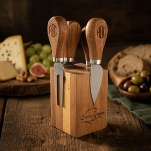 May include: A set of cheese knives with wooden handles featuring an engraved monogram, stored in a wooden block. The block displays the text "Dolor sit amer Lorem Ipsum" with a branch graphic. The knives have silver-toned metal blades.