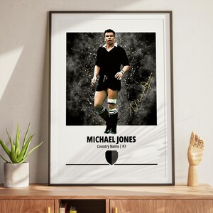 Könnte beinhalten: Gerahmter Druck mit Michael Jones in schwarzer Rugby-Uniform. Der Druck enthält seinen Namen, sein Land und seine Trikotnummer. Der Hintergrund hat einen dunklen, strukturierten Effekt mit einer Unterschrift.