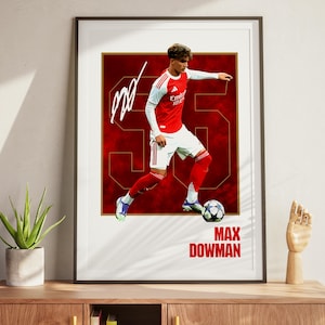 May include: Framed print of a soccer player in a red and white kit, kicking a soccer ball. The print has a red background with the number 35 and the name "MAX DOWMAN" in white. Includes a signature.